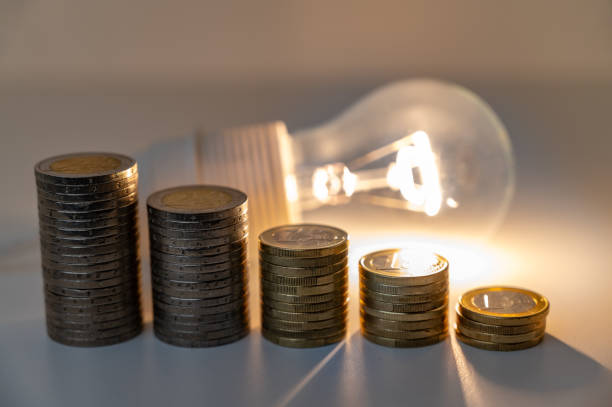 istock Lamp lit and pile of coins next to it. 1772653516