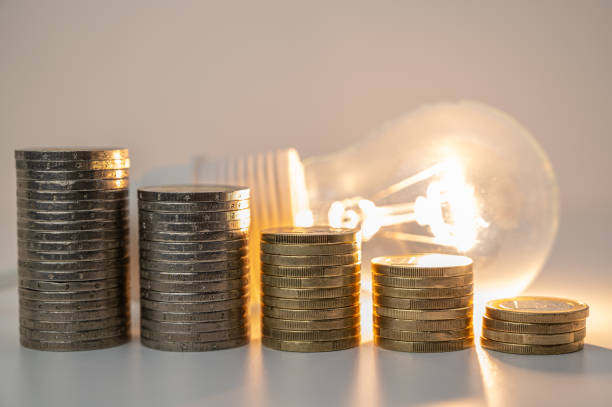 istock Lamp lit and pile of coins next to it. 1772653527