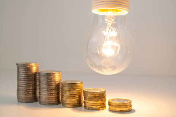 istock Lamp lit and pile of coins next to it. 1772653718