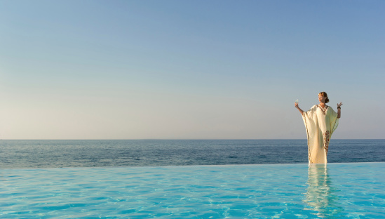 Woman in long dress like greek goddess posing near edge of infinity pool on a beach. Crete. Greece