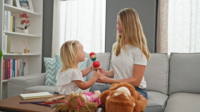 Confident caucasian mother and little daughter, a joyous duo, play maracas, dancing together at home, their smiles lighting up the living room.