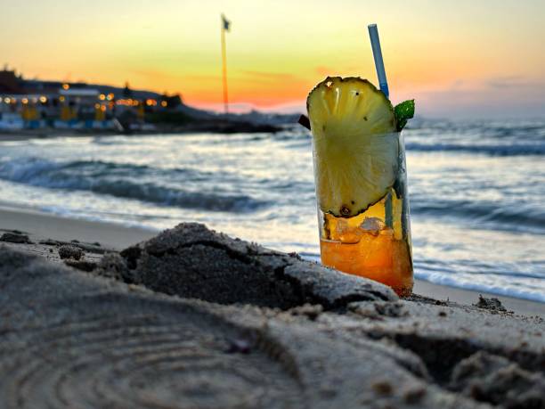 A refreshing beverage with a pineapple garnish on a sandy beach, with a large sailing vessel in the background