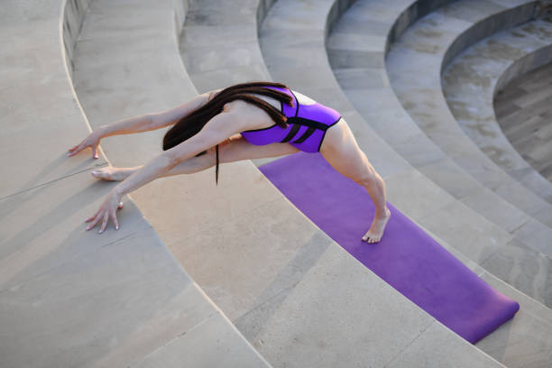 Studio shot of young woman in green outfit practicing happy bound angle yoga pose variation (baddha konasana variation) with playful expression on white background
