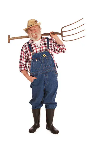 "Smiling senior farmer with straw hat, plaid shirt, bib overalls, lifting hay fork over one shoulder. Vertical layout, isolated on white background with copy space."