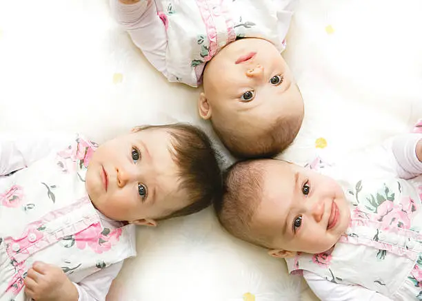 Close-up portrait of three babies lying on bed
