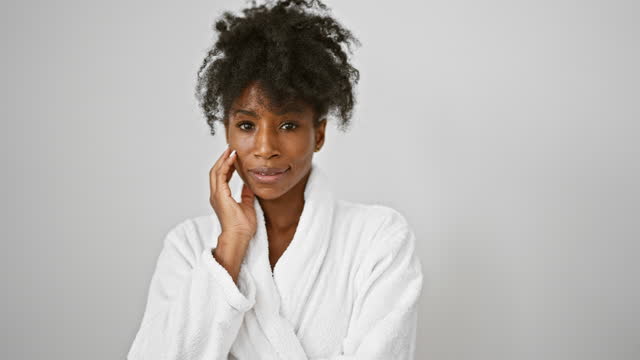 African american woman wearing bathrobe touching face over isolated white background