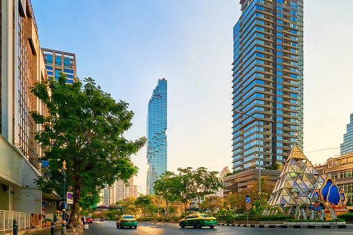Beautiful evening street in Bangkok, Thailand, with residential high-rises, palm trees, sunlight and sun glares, reflections. King Power Mahanakhon skyscraper in Silom district, tallest building in Thai kingdom.