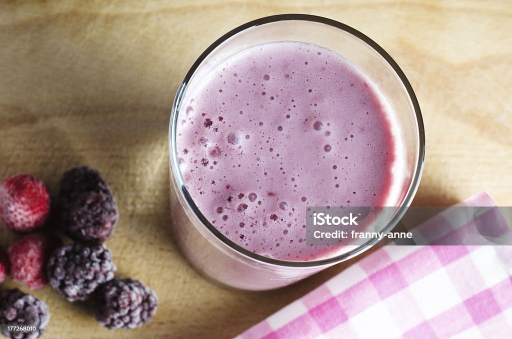 Summer Berry Soya Smoothie Overhead close up of a pink smoothie (made with soya milk)  on an old wooden chopping board with frozen Summer berries to the left and a gingham check napkin at bottom right. Berry Fruit Stock Photo