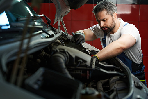 Serious focused automotive service technician tightening parts on customer vehicle with wrench