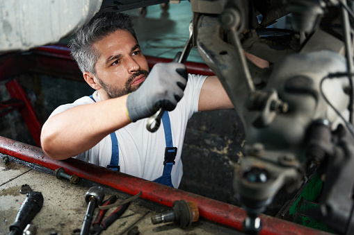 Serious car service technician is tightening nut on automobile underbody with wrench