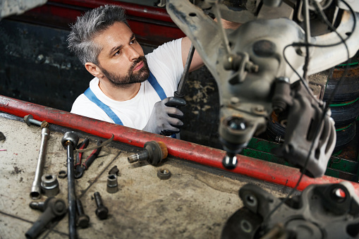 Serious automobile repair shop worker tightening parts on vehicle underside with spanner