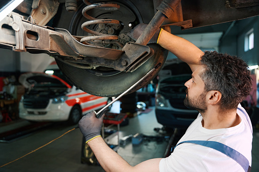 Serious focused Caucasian automotive service technician checking motor vehicle suspension system fasteners
