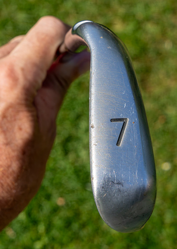 A golfer holding a 7 iron golf club above the fairway.