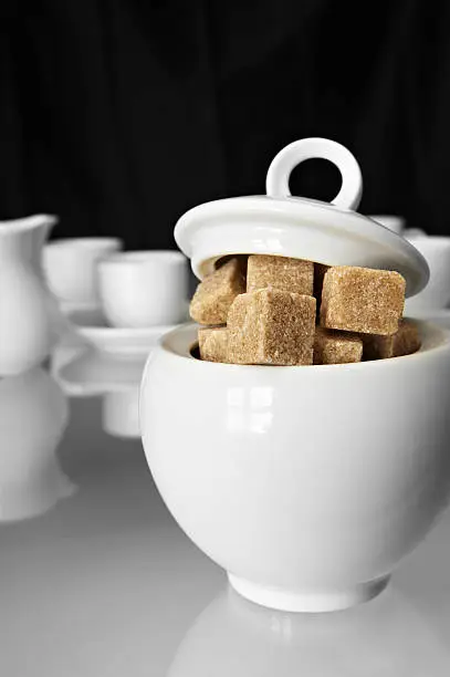 White sugarbowl with brown sugarcubes and some pottery on mixed black and white background