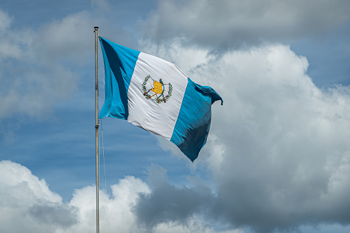 Guatemala, La Antigua - July 20, 2023: Closeup of national flag waving in wind against blue cloudscape