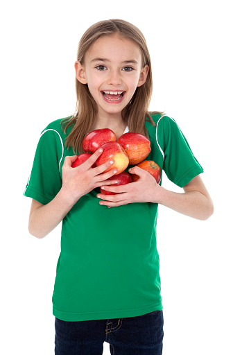 Front view of pretty little girl holding several apples on white background.
