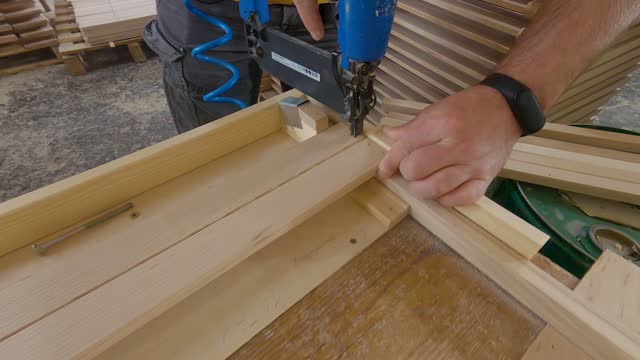 Craftsman in a carpentry workshop hammers nails with a pneumatic hammer. Making a stool