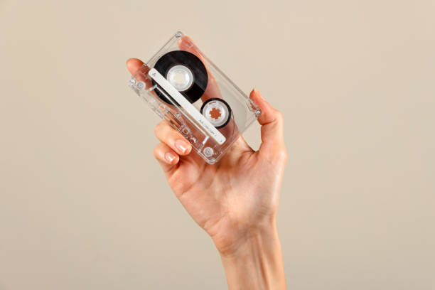 istock Unrecognizable woman hand holding retro cassette against beige backdrop in light 1772720337