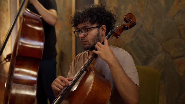 Young adult student playing cello in music studio