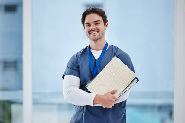 médico, braços cruzados e retrato de homem feliz com caderno, prontuários ou informações clínicas para teste de estudo. estágio de cirurgião, educação médica e estudante de enfermagem confiante para a pesquisa em medicina - medical student healthcare and medicine book education - fotografias e filmes do acervo