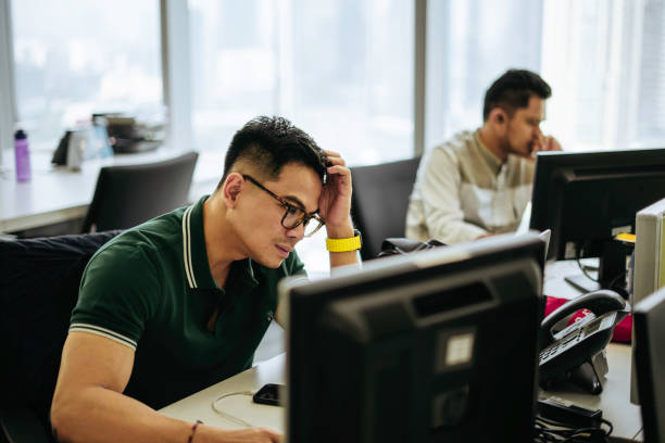 plan d’un jeune homme d’affaires qui a l’air stressé tout en travaillant dans un bureau moderne - frustration computer men emotional stress photos et images de collection