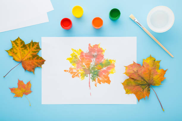 istock Painting and copying colorful leaf pattern with gouache color on white paper. Light blue table background. Pastel color. Closeup. Top down view. 1772745881