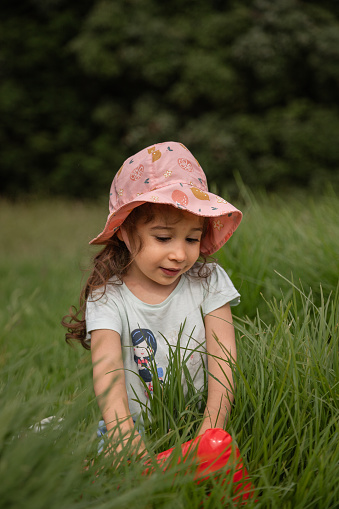 Concept of happy childhood, exploring the world around you. Loving girl playing on the grass in a park during the day.