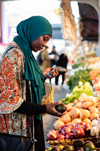 Muslim black woman at public market in autumn. She is in her late thirties, from african descent and is wearing a deep green hijab. Vertical waist up outdoors shot. This was taken in Montreal, Quebec, Canada.