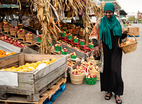 Muslim black woman at public market in autumn. She is in her late thirties, from african descent and is wearing a deep green hijab. Horizontal full length outdoors shot. This was taken in Montreal, Quebec, Canada.