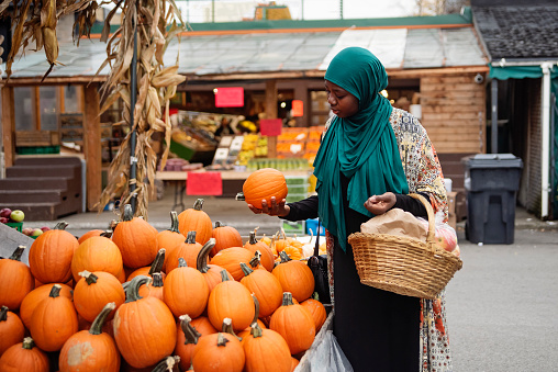 Muslim black woman at public market in autumn. She is in her late thirties, from african descent and is wearing a deep green hijab. Horizontal waist up outdoors shot. This was taken in Montreal, Quebec, Canada.