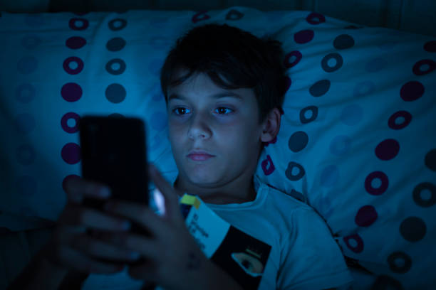 夜、暗闇の中で本とスマートフォンを持ってベッドにいる子供。若い年齢でのモバイル依存症の問題の概念。電子機器の使用による睡眠障害や不眠症の子供 - child bedtime imagination dark ストックフォトと画像
