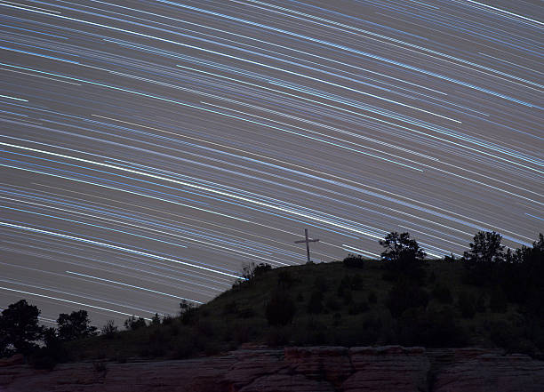 Star trails above cross on hill stock photo