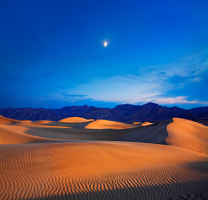 Early Morning Sunlight Merges With A Twilight Moon Over Sand Dunes And Mountains At Death Valley National Park, California, USA