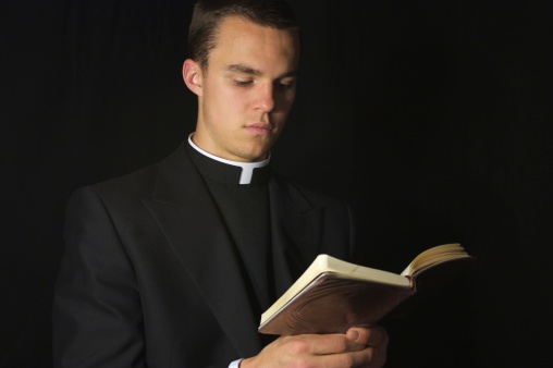 Young Priest in black reading prayer book