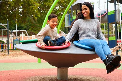 Latin lesbian couple laughing while playing with their son in the children's playground. LGBT family.
