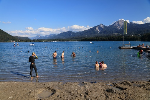 Tourists enjoy the summer at Lake Faak (Faaker See) with view of Karawanks mountain range (Karawanken) in Austria.