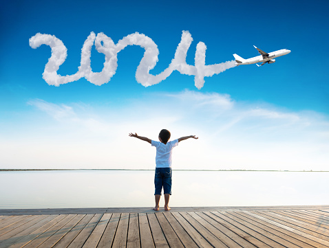 Boy arms outstretched with plane writing new year number 2024 in the sky