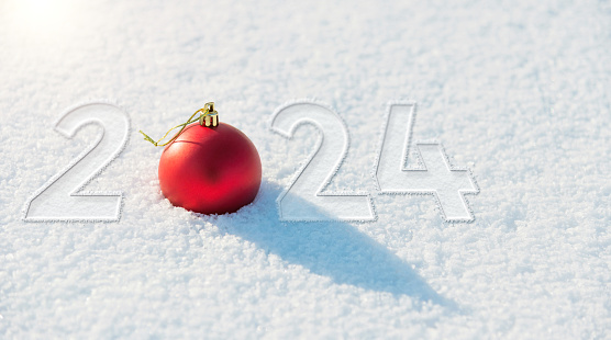New year number 2024 written on snowfield with red christmas ball