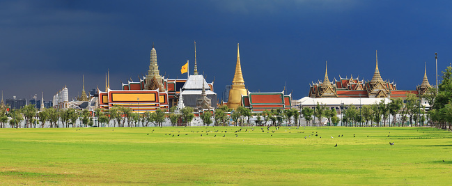 The beautiful panorama view of the famous temple of the Emerald Buddha and the Grand Palace in Bangkok, Thailand, with the green grass is in the foreground and the blue sky in the background.