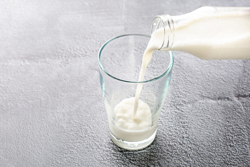 Fresh milk from pitcher pouring into glass with splashing isolated on white background.