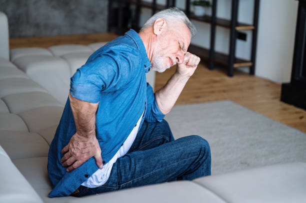 Mature man suffering from backache and hold his back Unhappy mature man feeling bad, suffering from backache, hold his back and can't stand up from sofa. Middle aged male with discomfort and kidney disease sitting alone on couch at home low quality of life stock pictures, royalty-free photos & images