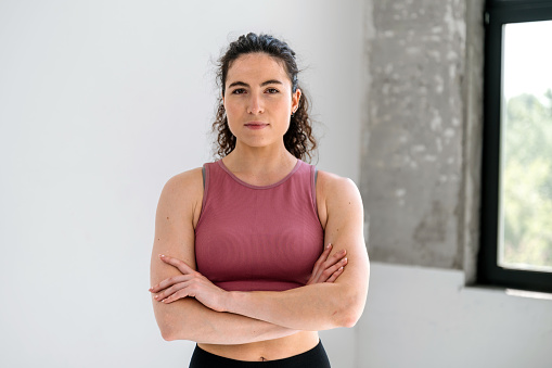 Healthy lifestyle concept. Waist up portrait of athletic woman in sportswear with crossed arms after working out at home or in a club. Confident fitness instructor looking at camera.