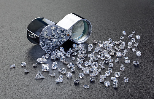 Loose diamonds next to a 10x  magnifier glass with reflection of the diamonds in the magnifier glass