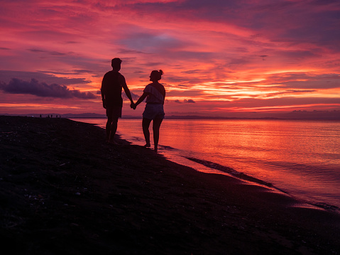 Silhouette of couple on beach at dusk under a spectacular sky