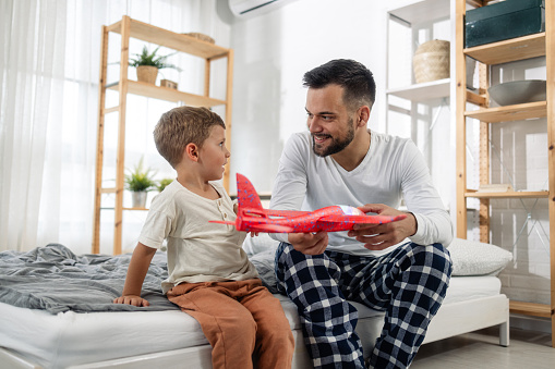Young man and his son playing in bedroom with an airplane toy