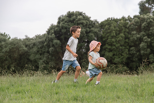 Two children playing with a ball in the green park. Concept of happy childhood in contact with nature, healthy lifestyle.