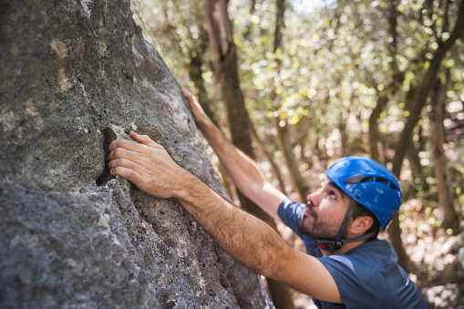 Close-up of a climber with a protective helmet gripping the rock with one hand. Outdoor climbing concept.