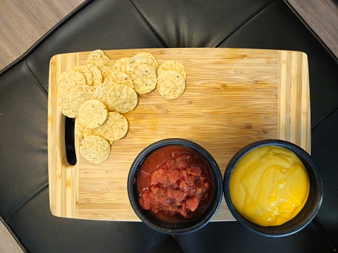 Overhead Shot Of Salsa And Queso Dip With Nacho Chips Sitting On A Wood Cutting Board