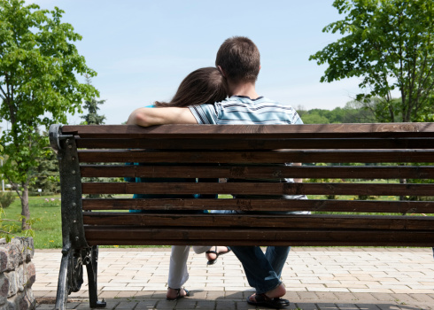 Young couple sitting on bench in park. Rear view.