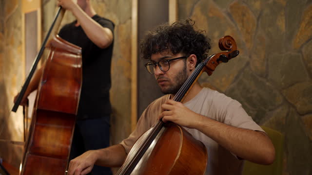 Two young adult students playing cellos in music studio
